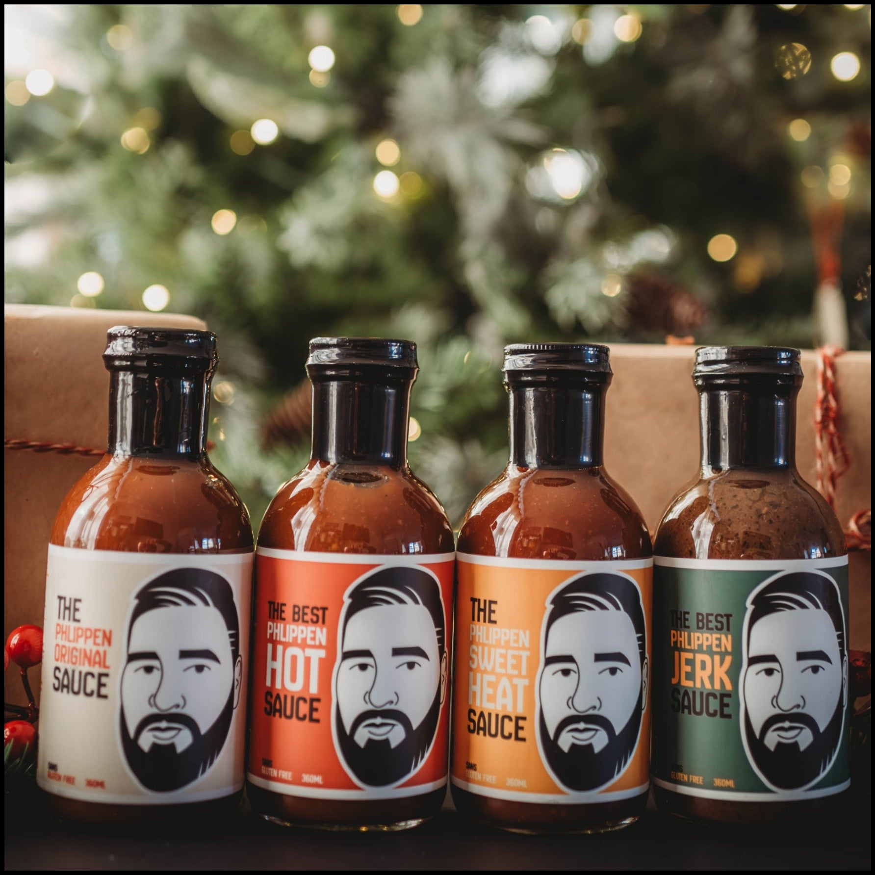 Four bottles of Phlippens sauce with face designs on labels in front of a decorated Christmas tree.