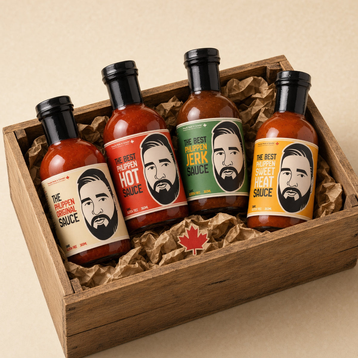 Four sauce bottles in a wooden gift box with crumpled brown paper. The bottles have black caps and colourful labels featuring a stylized bearded man's face, with text showing the flavours.